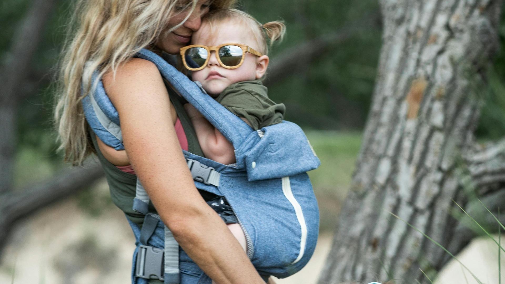 Maman portant son bébé dans un porte-bébé en plein air, lumière naturelle dorée